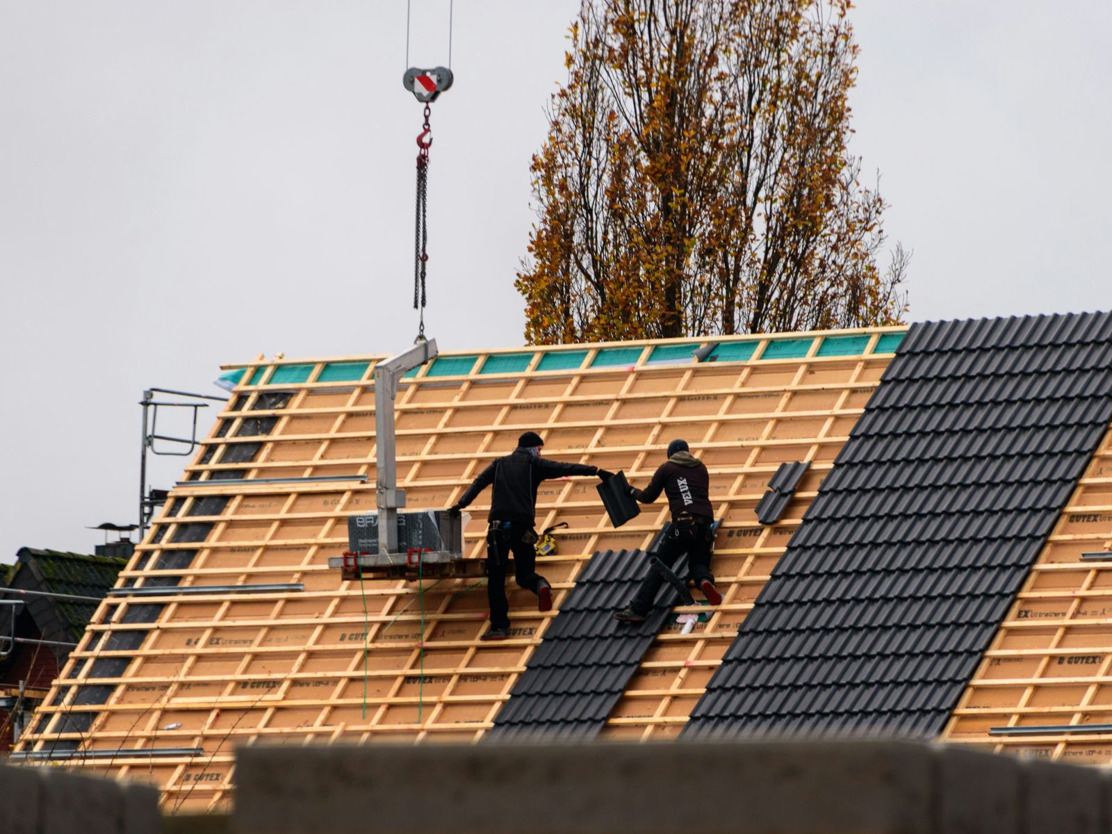 Two roofers laying dark grey tiles across the battens of a new pitched roof